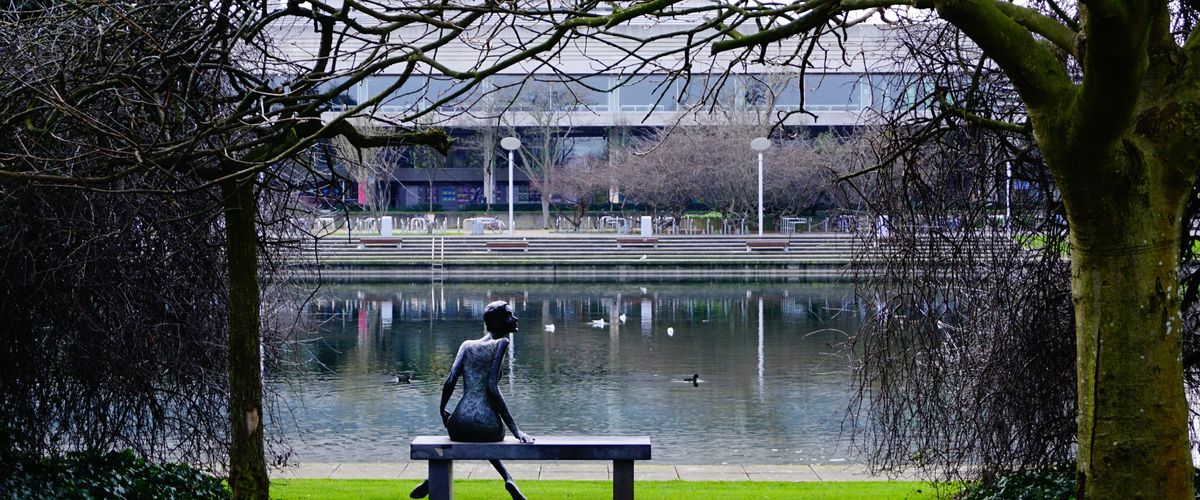 Sculpture of woman sitting on a bench looking at a pond