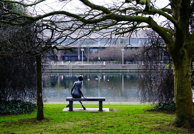Sculpture of woman sitting on a bench looking at a pond