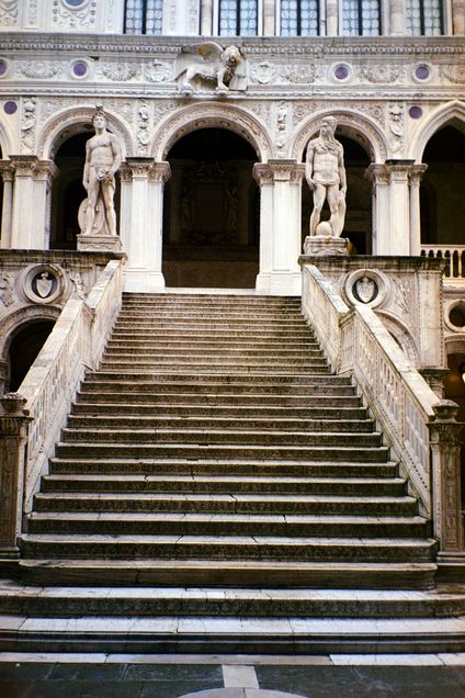 Steps leading up to building with two statues of ancient men at the top and of a griffen over an arched doorway in venice italy