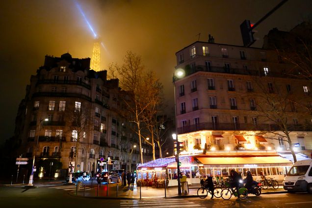 night view of a paris street with the to of the eiffel tower and its spot light in view