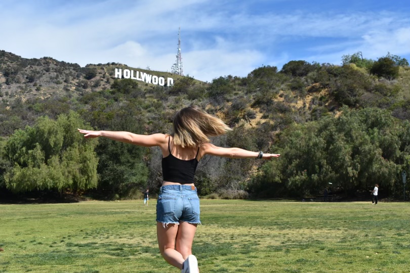 Woman with her back to the camera with arms spread wide with the Hollywood sign in the foreground