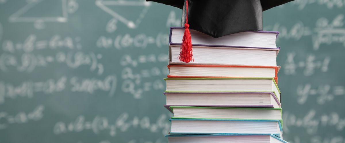 Graduation cap on a stack of books in front of a chalkboard