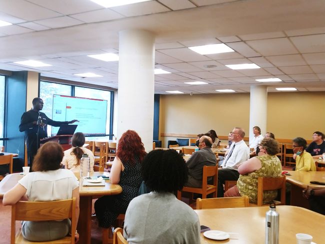 Mr. Sarr standing to present his work to seated BU Libraries staff