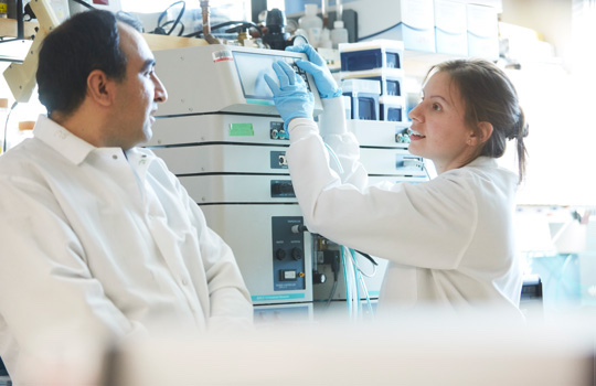 Two people wearing lab coats operating machinery in a lab