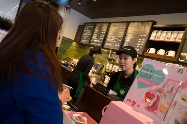 Barista Kim Jung Mi, a mother who had left the workforce seven years ago and is now employed by Starbucks Coffee Korea Co. under its "returning-mom" program, right, serves a customer at one of the company's stores in Gimpo, South Korea, on Friday, March 7, 2014. Starbucks Korea's "returning-mom" program is part of a drive to raise female participation in Asia's fourth-largest economy as the nation's first female leader, President Park Geun Hye, tries to counter the effects of an aging population. Photographer: SeongJoon Cho/Bloomberg via Getty Images