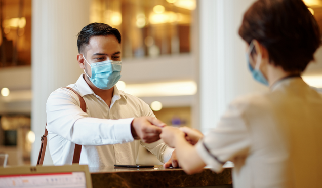 Hotel receptionist giving digital room key to guest in medical mask
