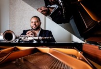 Jimmy Greene poses at the piano with saxophone