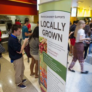 Boston University students file past a "Locally Grown" sign in a BU dining hall. BU Dining Services hit its goal of providing 20% sustainable food three years early.