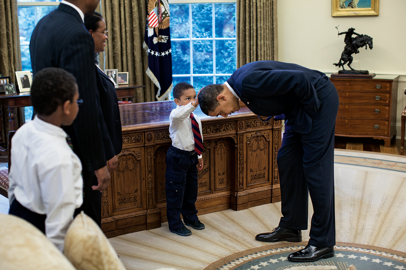 Photograph entitled Hair Like Mine taken by official White House photographer Pete Souza of President Barack Obama bending down so a young African American boy can touch his head.