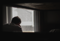 image of a man staring out of a window sitting in a dark room.