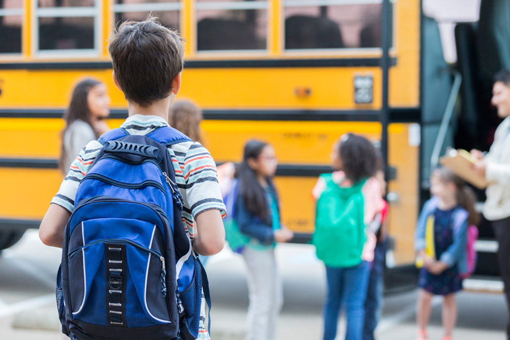 A child watches as students get on a yellow school bus 