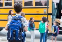 A child watches as students get on a yellow school bus