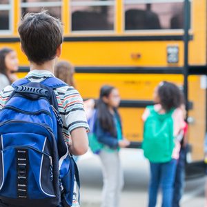 A child watches as students get on a yellow school bus