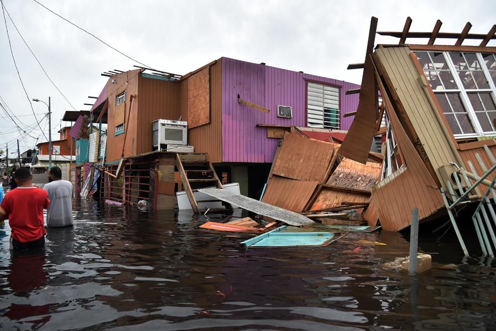 People walk in a flooded street next to damaged houses in Juana Matos, Catano, Puerto Rico, on September 21, 2017, after Hurricane Maria