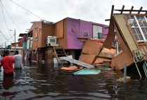 People walk in a flooded street next to damaged houses in Juana Matos, Catano, Puerto Rico, on September 21, 2017, after Hurricane Maria