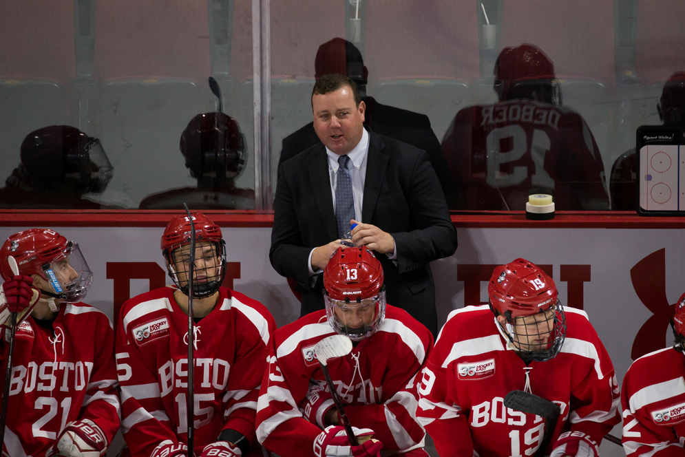 BU men's ice hockey head coach Albie O'Connell talks to a player on the bench during a game.