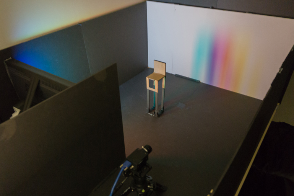 A rainbow penumbra on a far wall is created by a bright scene displayed on an LCD monitor (left) and a chair (center).