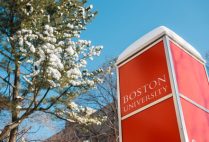 Boston University sign with snow on top in front of a snowcovered tree