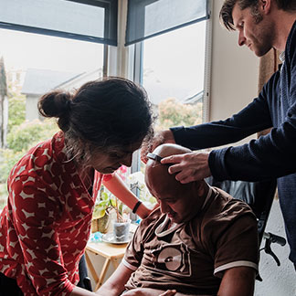 Craig Cloutier and Rahul Desikan’s wife, Maya Vijayaraghavan, put on Rahul's head mouse and help him get ready to work at his desk.