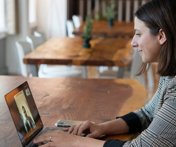 Woman sitting at a table looking at video meeting on a laptop
