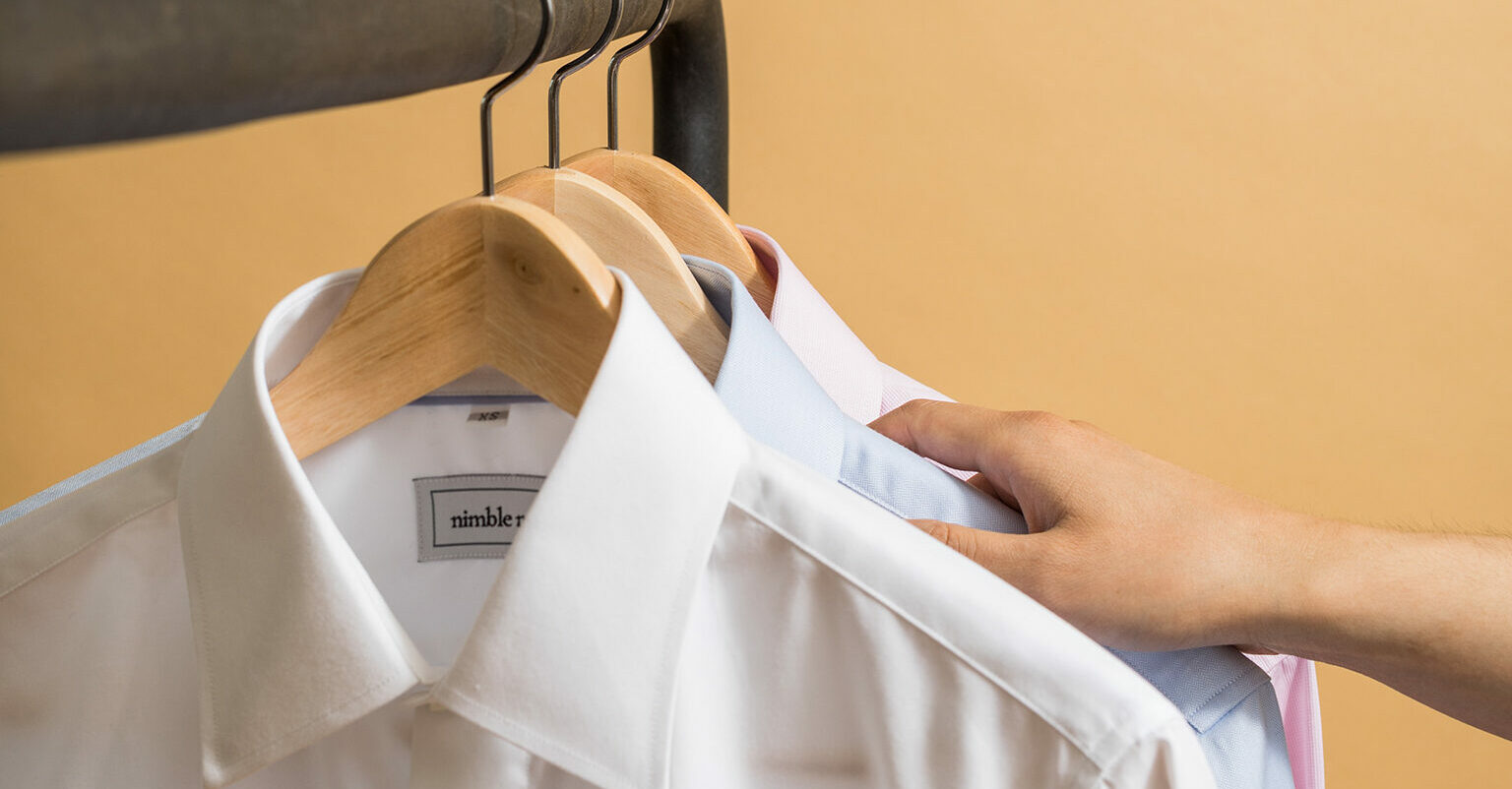 A hand reaches for button down shirts on hangers
