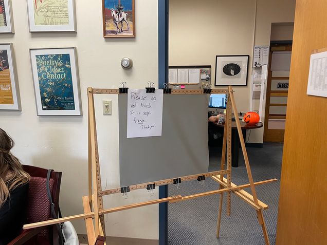 A scrim sits on an easel with a "do not touch" sign.