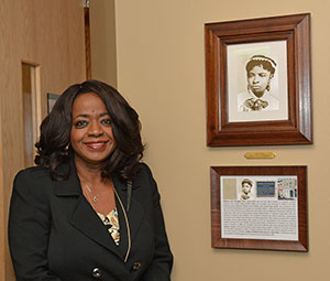 Melody T. McCloud standing next to framed photograph and article about Rebecca Lee Crumpler