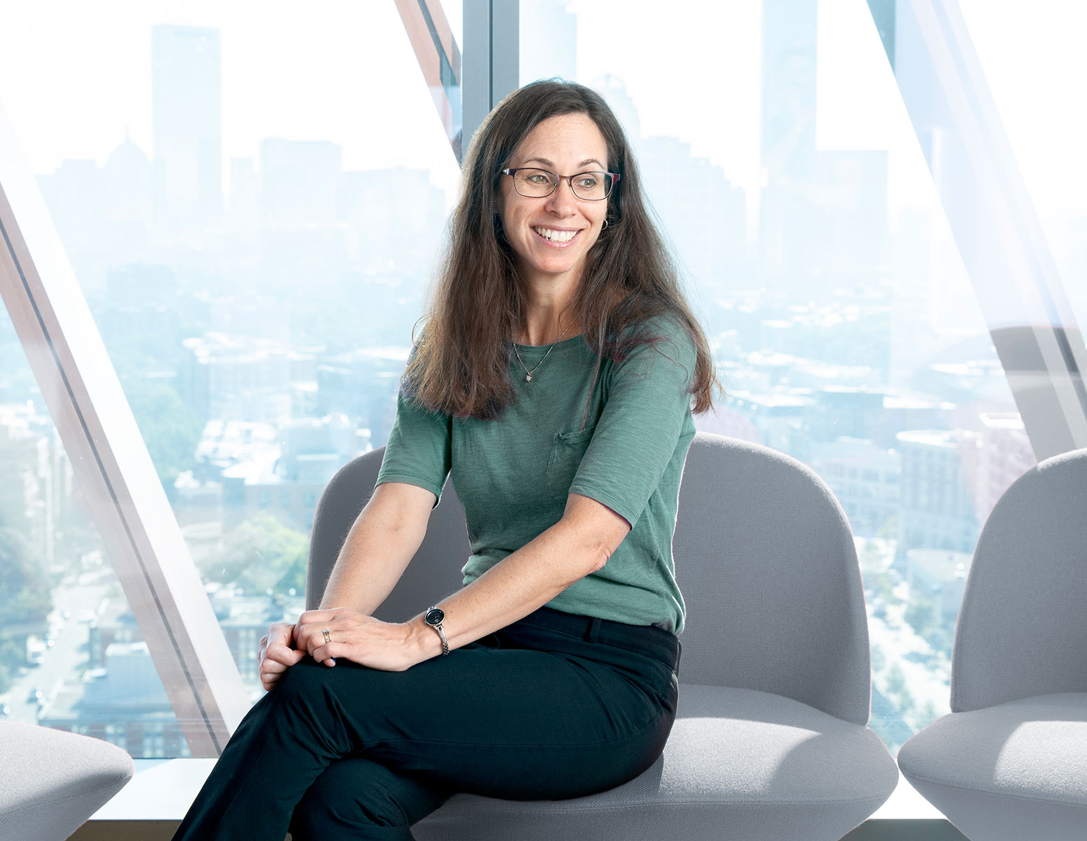 Pam Templer sitting in a chair in front of a wall of windows