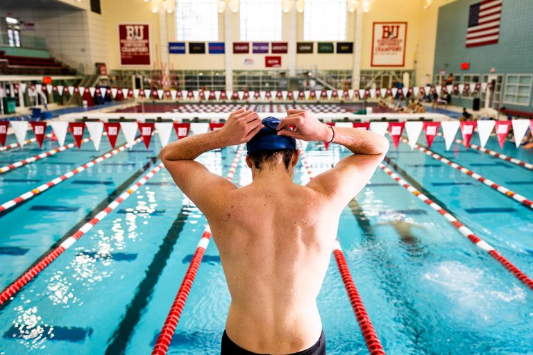 Back of MAle swimmer sitting on edge of pool adjusting bathing cap