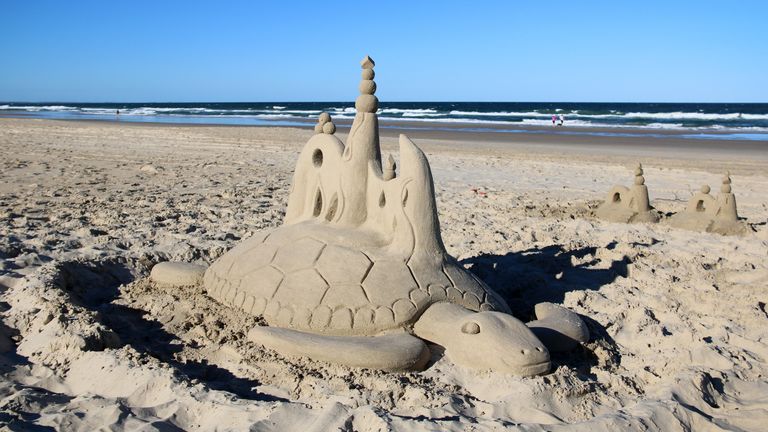 picture of a sand sculpture at the beach of a turtle with a castle on its back