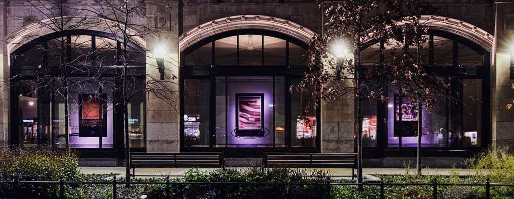 The exhibition As, Not For: Dethroning Our Absolutes as seen through the Stone Gallery’s new floor-to-ceiling windows at night.