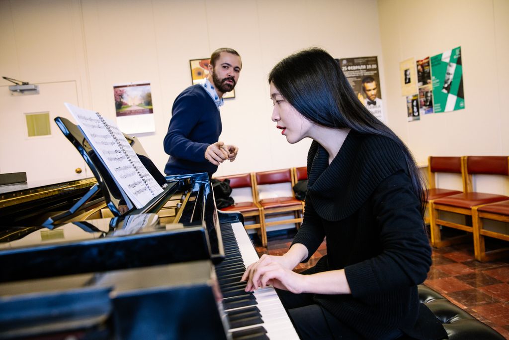 Student musician playing the piano, supervised by piano instructor