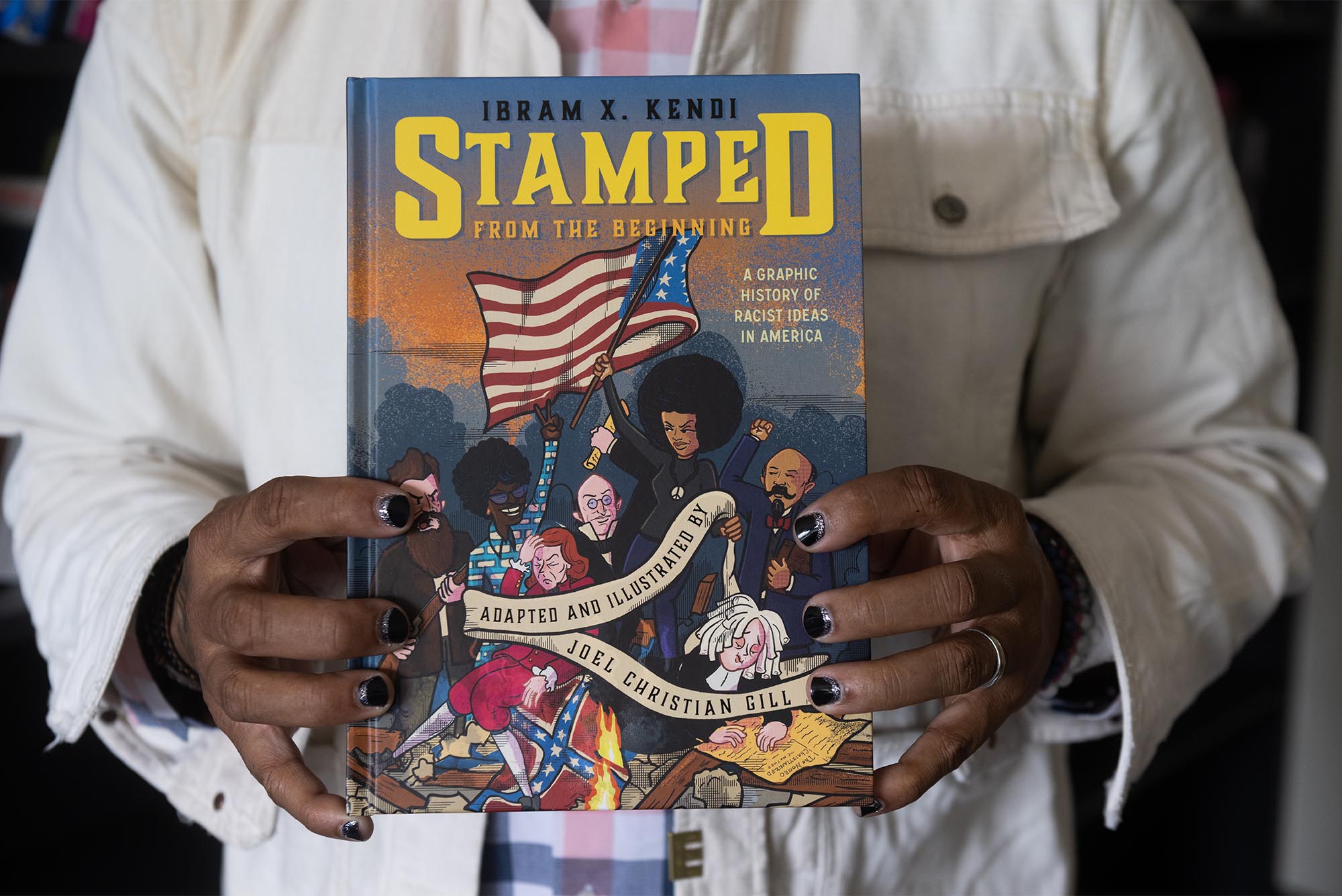 Joel Christian Gill holding the graphic book Stamped From the Beginning