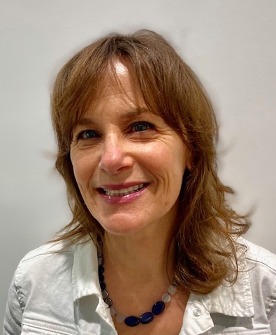 Portrait of Barb Raney, Boston University School of Music Assistant Director, Student Services, and Academic Advisor for CFA undergraduate music students, with shoulder-length light brown hair wearing a white collared shirt and a necklace with blue and light-colored beads. The background is a plain light color.