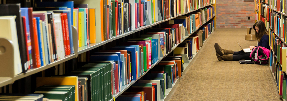 picture of several book shelves filled with books and a woman sitting on the floor reading a book