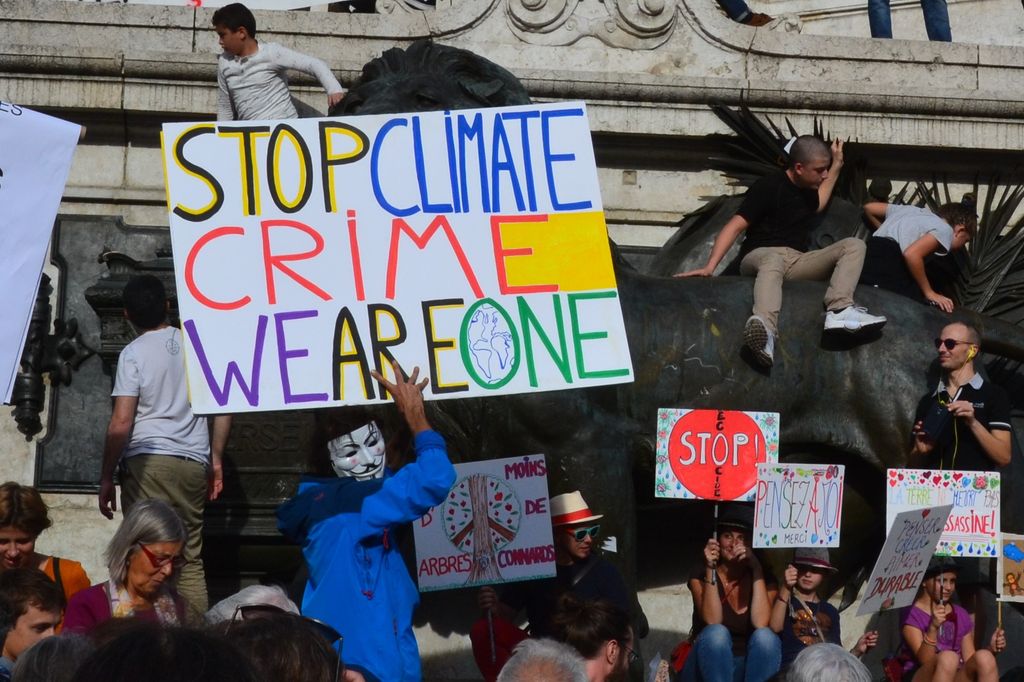 Climate change protesters surround a statue, holding signs in French and English: "Stop Climate Crime We Are One," "Stop Ecocide," 