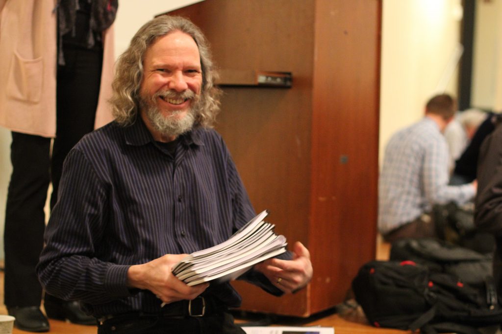 CGS Associate Professor Robert Schoch holding a stack of bound Capstone projects and smiling