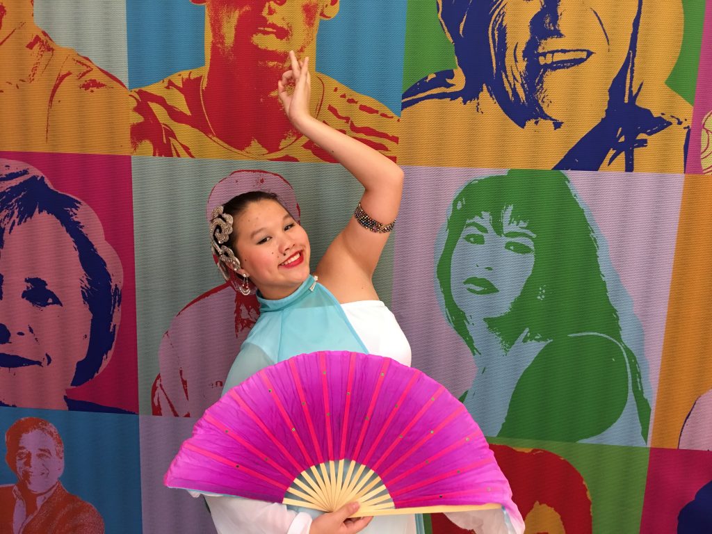 Natalie Seara in a colorful dance costume holding a bright pink fan