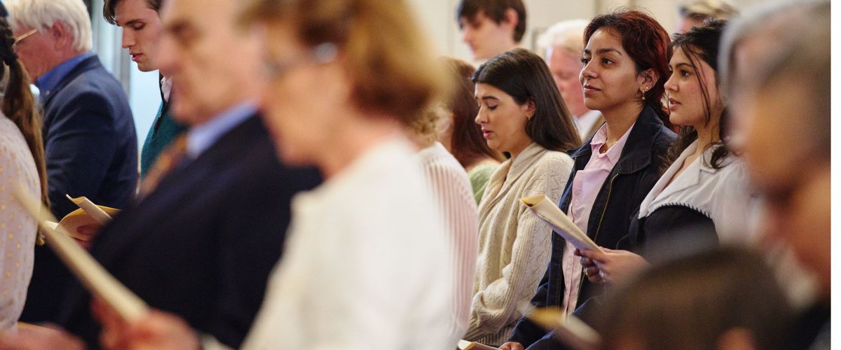 Close up photo into the chapel congregation. The photo focuses on three young women, likely students, smiling and looking toward the front of the room.