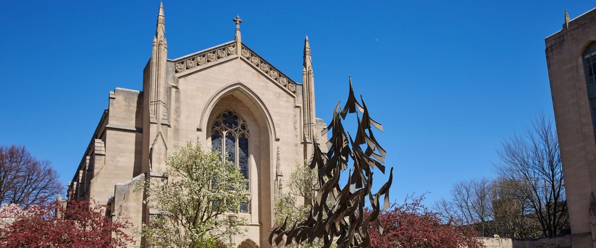 The font of Marsh Chapel pictured with blooming trees and a bright, clear sky. The MLK "Free at last" statue is partially visible in the foreground.