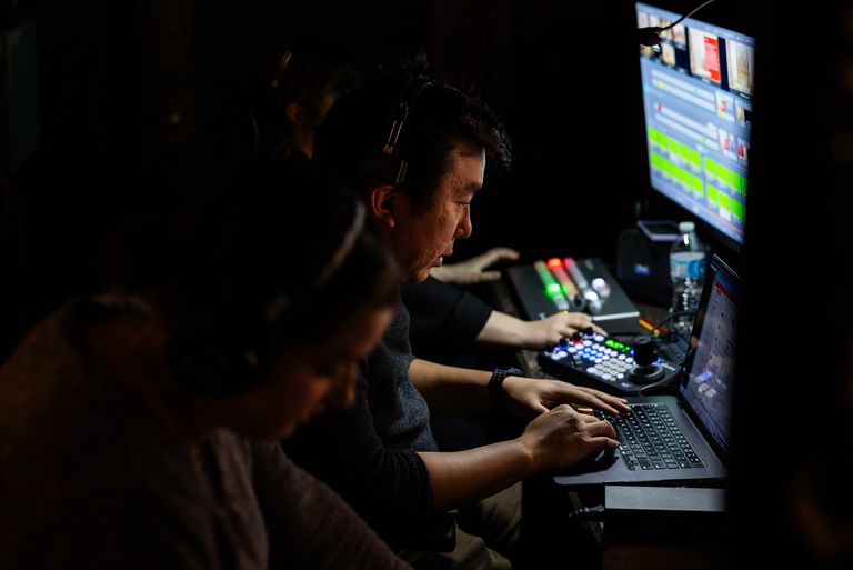Jin Choi sits at the controls of the livestream in a darkened media studio