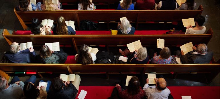 Image taken looking down from the chapel balcony into the pews. People sit in rows holding worship bulletins.