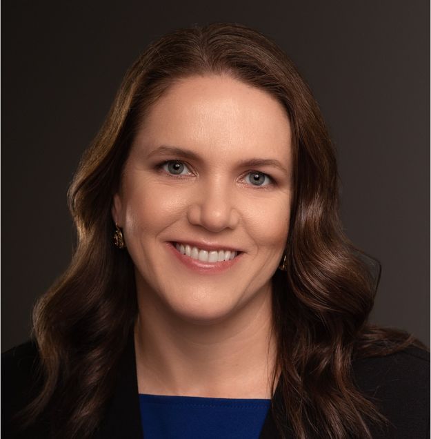 woman with shoulder length wavy brown hair smiling wearing a navy blue top