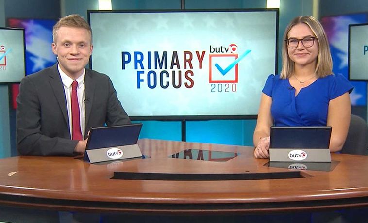 Students at anchor desk in TV studio.