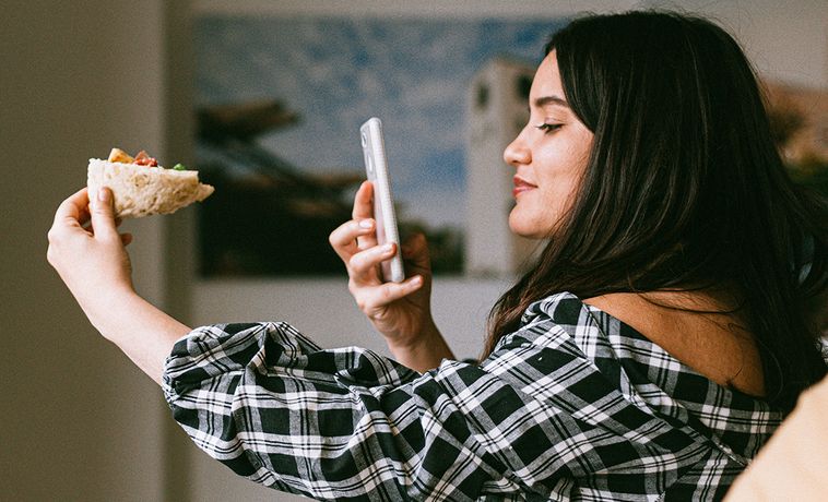 Woman photographing slice of pizza with her phone.