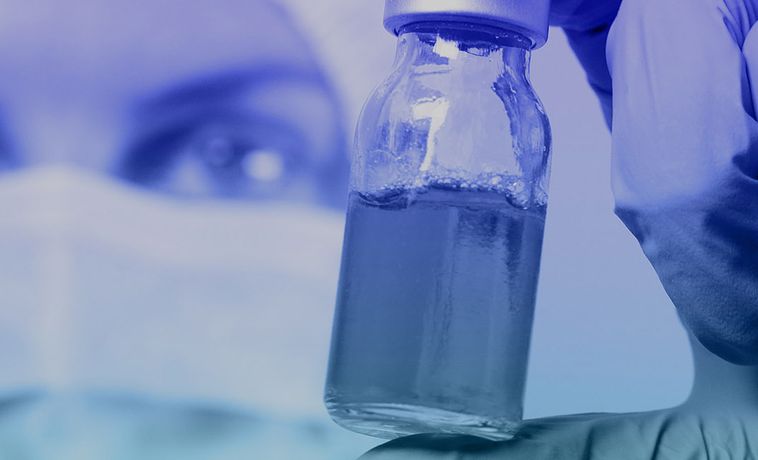 Close-up of vial of liquid held in gloved hand.