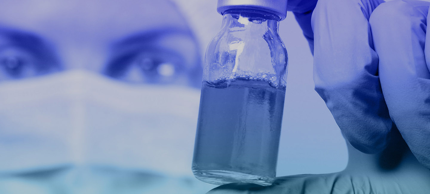 Close-up of vial of liquid held in gloved hand.