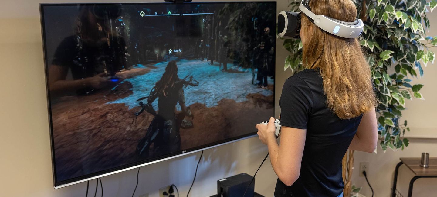 Woman shown from behind, wearing a VR headset while playing a video game.