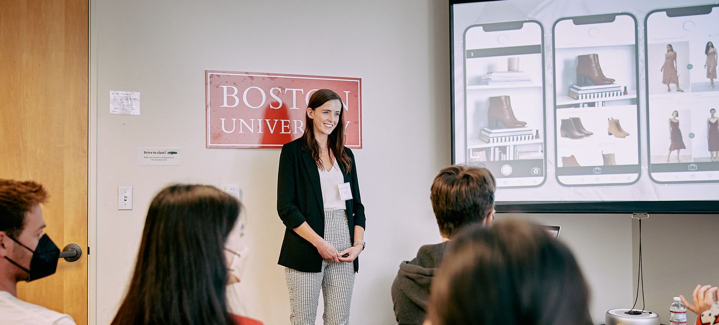 Woman presenting in front of a screen in a room of colleagues.