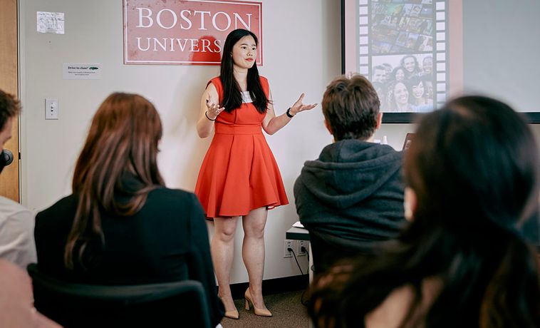 Woman in red dress speaking in front of small gathering during PitchFest 2022.